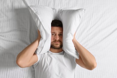 Photo of Sleepy man covering his ears with pillow in bed, top view. Insomnia problem