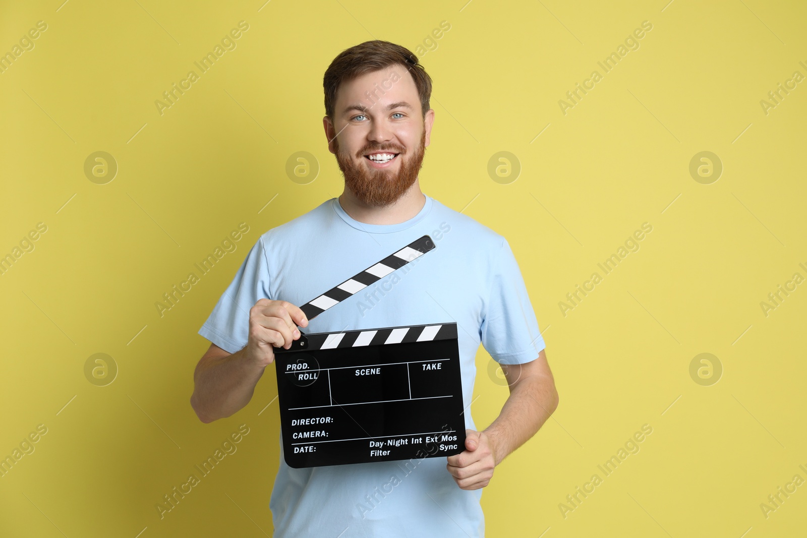 Photo of Making movie. Smiling man with clapperboard on yellow background