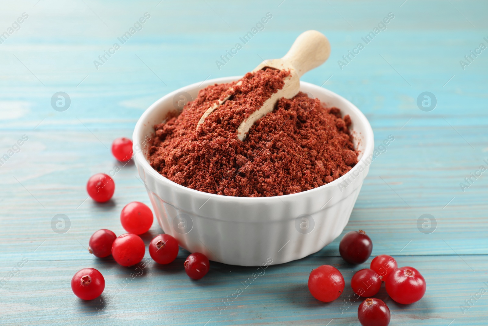 Photo of Cranberry powder in bowl, scoop and fresh berries on light blue wooden table, closeup