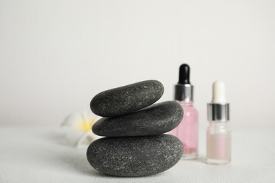 Stack of grey spa stones, oils and flower on white table