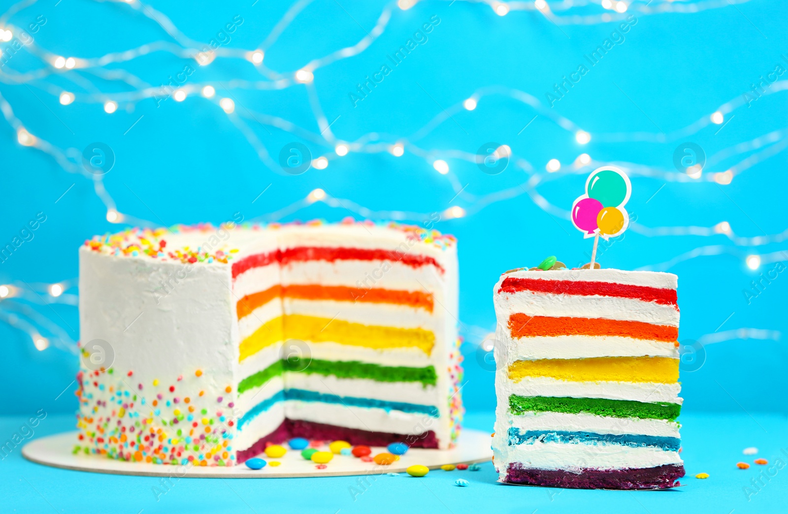 Photo of Delicious rainbow cake on table against blurred lights