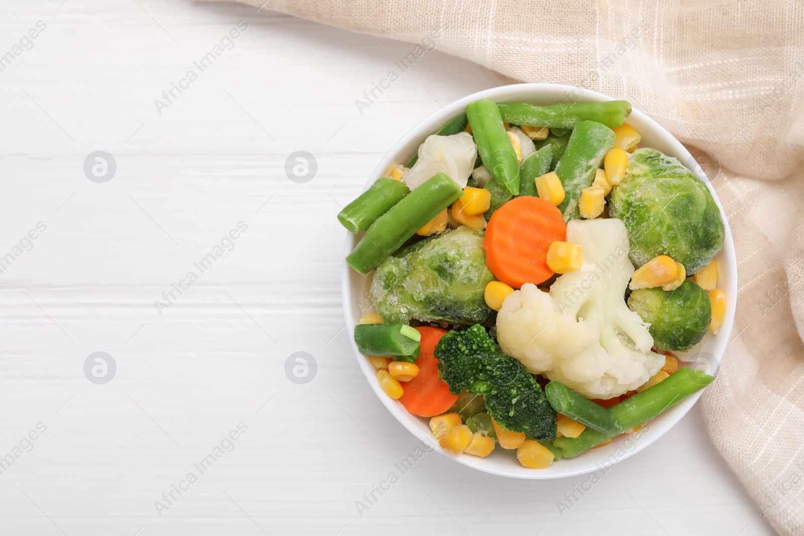 Photo of Mix of different frozen vegetables in bowl on white wooden table, top view. Space for text