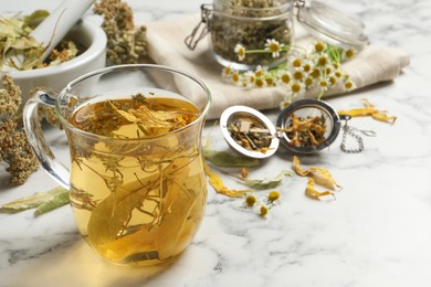 Photo of Freshly brewed tea and dried herbs on white marble table. Space for text