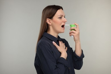 Woman using throat spray on grey background