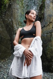 Photo of Beautiful young woman in stylish bikini near waterfall outdoors, low angle view