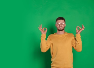 Photo of Young man meditating on green background, space for text. Zen concept