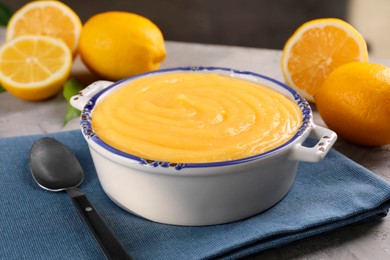 Delicious lemon curd in bowl, fresh citrus fruits and spoon on table, closeup