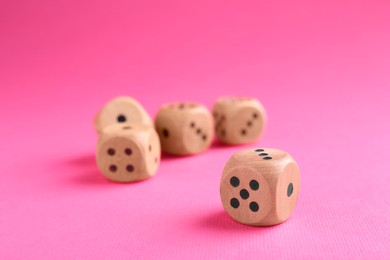 Many wooden game dices on pink background, closeup