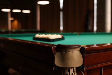 Balls in triangle rack on green table indoors, focus on billiard pocket. Space for text