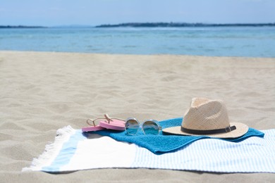 Blanket with towel, flip flops, hat and sunglasses on sandy beach near sea, space for text