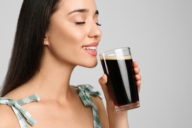 Photo of Beautiful woman with cold kvass on light grey background, closeup. Traditional Russian summer drink