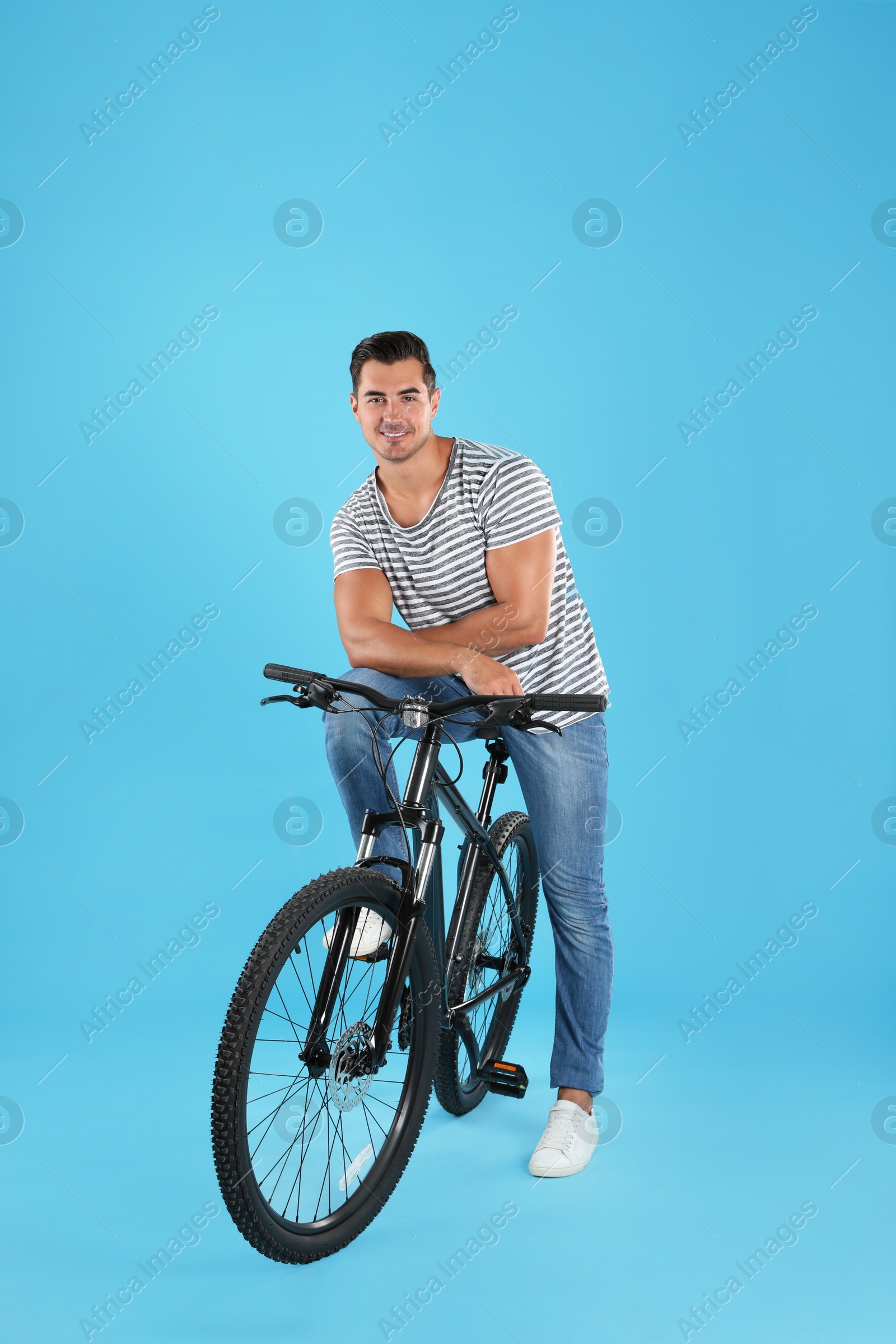 Photo of Handsome young man with modern bicycle on light blue background