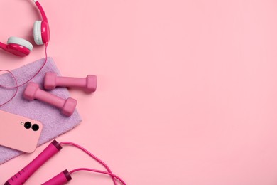 Flat lay composition with dumbbells and smartphone on pink background. Space for text