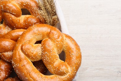 Delicious pretzels with sesame seeds and wheat spikes on white wooden table, top view. Space for text