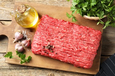 Photo of Raw ground meat, spices, parsley and oil on wooden table, top view