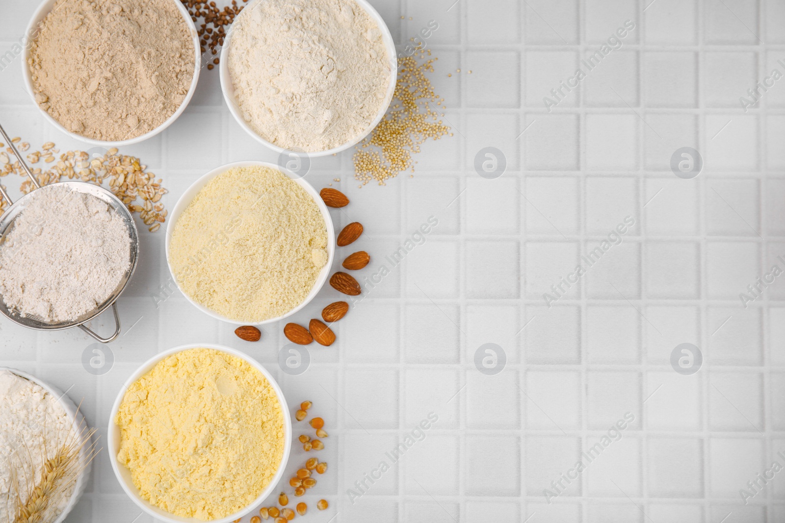 Photo of Bowls with different types of flour and ingredients on tiled table, flat lay. Space for text