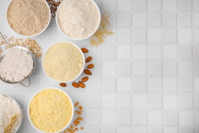 Bowls with different types of flour and ingredients on tiled table, flat lay. Space for text