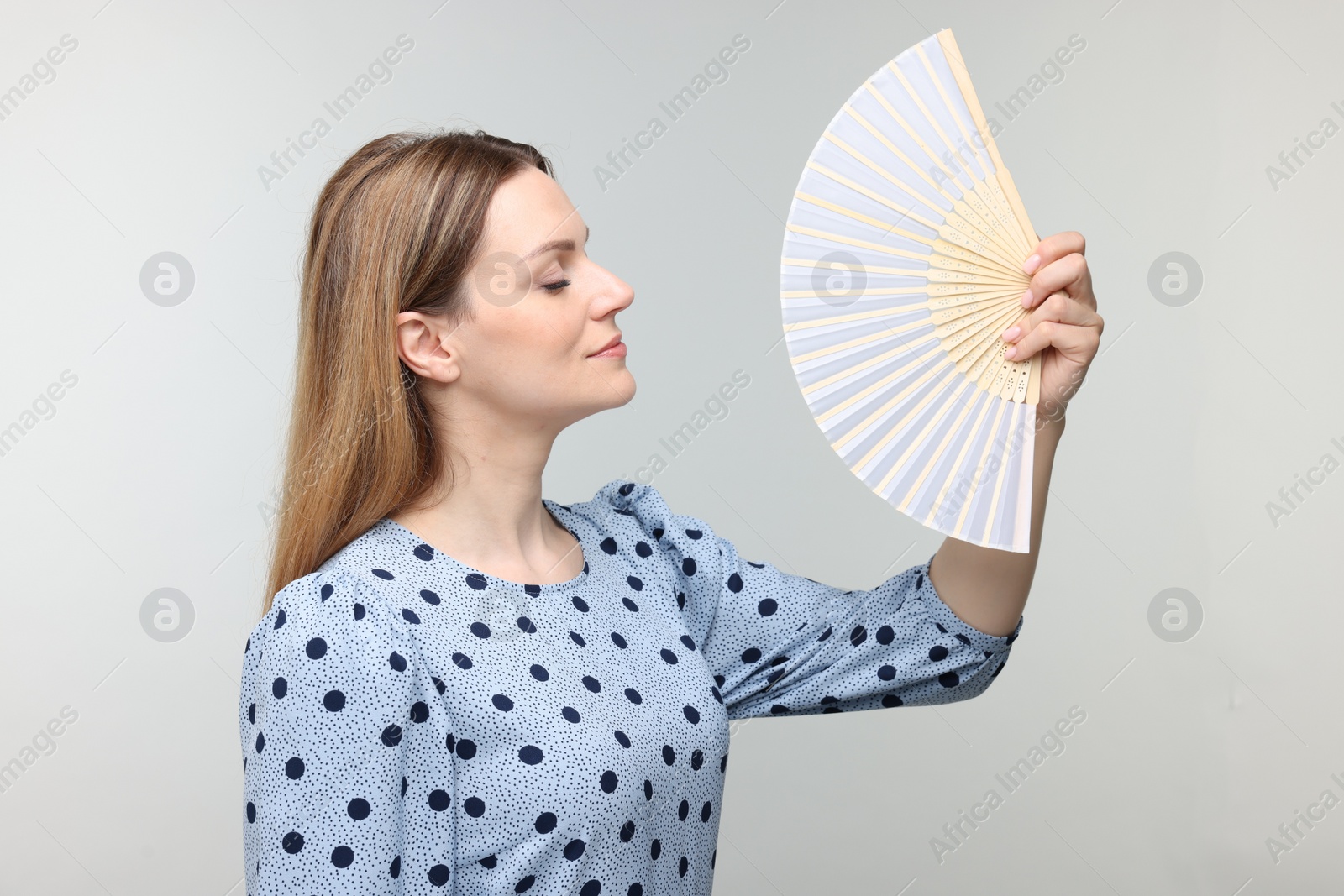 Photo of Beautiful woman waving hand fan to cool herself on light grey background