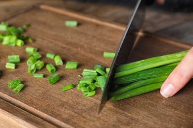 Photo of Woman cutting fresh green onion on wooden board at table, closeup