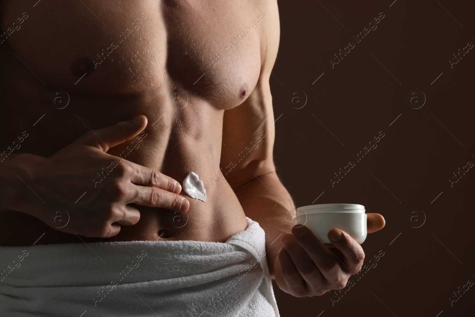 Photo of Man applying moisturizing cream onto his body on brown background, closeup