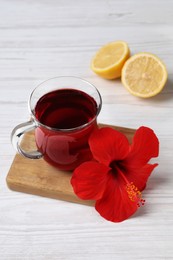 Photo of Delicious hibiscus tea, halves of lemon and beautiful flower on white wooden table