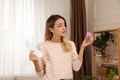 Photo of Young woman with menstrual cup and disposable pad at home