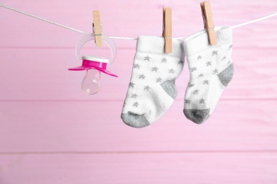 Photo of Pair of socks and pacifier on laundry line against pink wooden background. Baby accessories