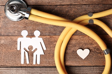 Photo of Flat lay composition with heart, stethoscope and paper silhouette of family on wooden background. Life insurance concept