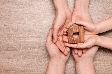 Photo of Home security concept. Family holding house model at wooden table, top view with space for text