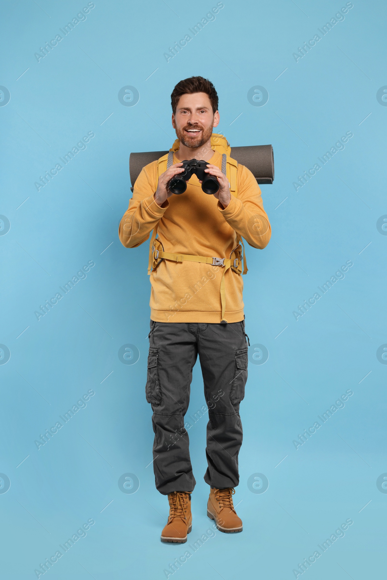 Photo of Man with backpack and binoculars on light blue background. Active tourism