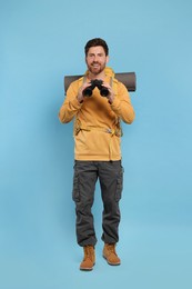 Photo of Man with backpack and binoculars on light blue background. Active tourism
