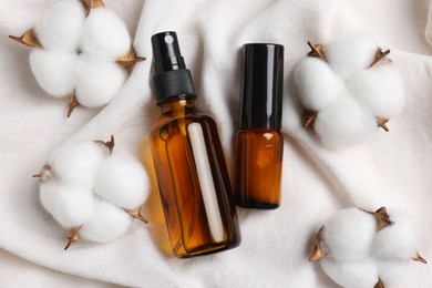 Photo of Bottles of organic cosmetic products and cotton flowers on white fabric, flat lay