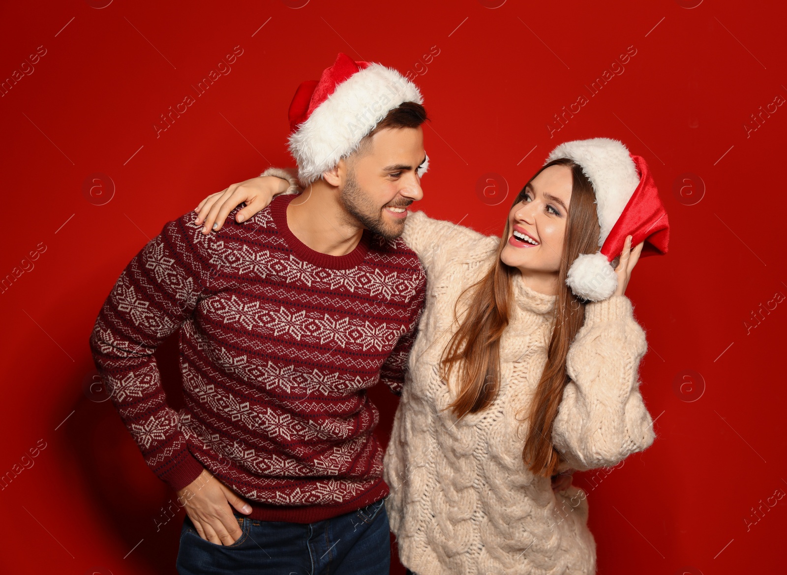 Photo of Couple wearing Christmas sweaters and Santa hats on red background