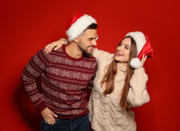 Couple wearing Christmas sweaters and Santa hats on red background