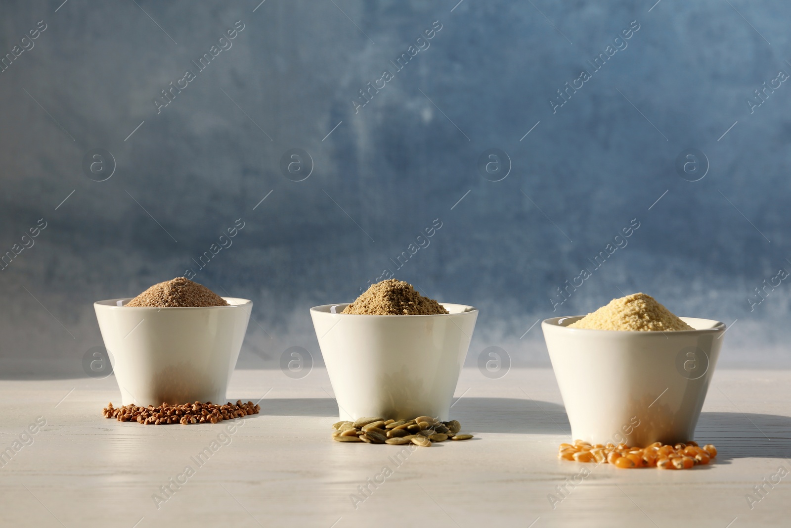 Photo of Bowls with different types of flour and seeds on table against color background. Space for text