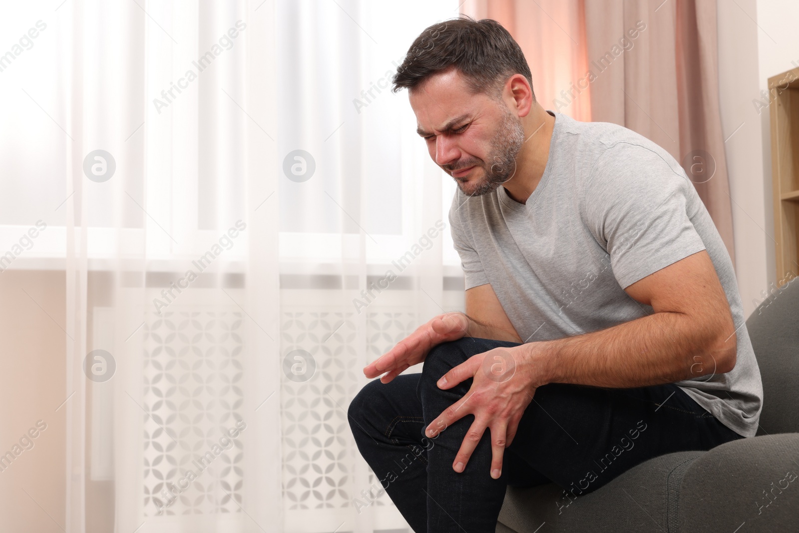 Photo of Man suffering from knee pain on sofa indoors