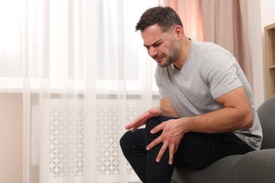 Man suffering from knee pain on sofa indoors