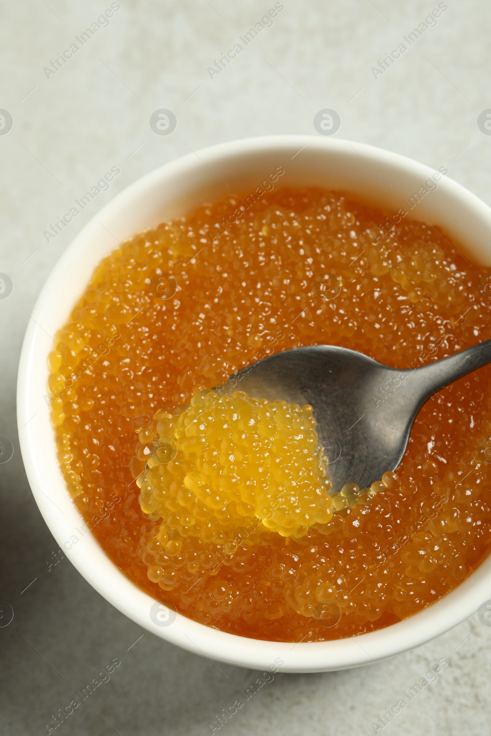 Photo of Fresh pike caviar in bowl and spoon on light grey table, top view