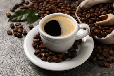 Cup of aromatic hot coffee and beans on grey table