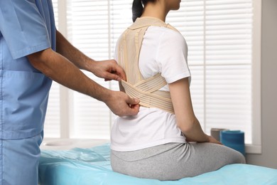 Photo of Orthopedist helping patient to put on posture corrector in clinic, closeup. Scoliosis treatment