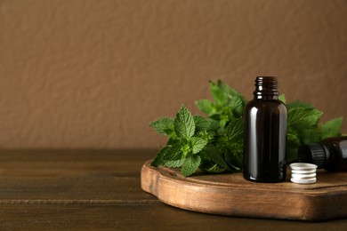 Photo of Glass bottle of nettle oil and fresh leaves on wooden table against brown background, space for text