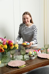 Photo of Woman setting table for festive Easter dinner at home