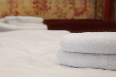 Clean folded towels on bed in hotel room, closeup. Space for text