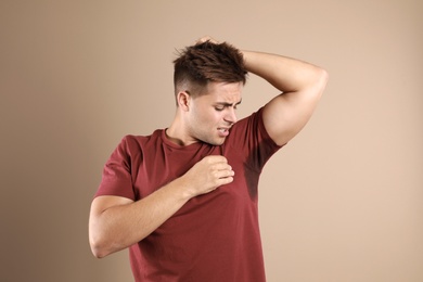Young man with sweat stain on his clothes against beige background. Using deodorant