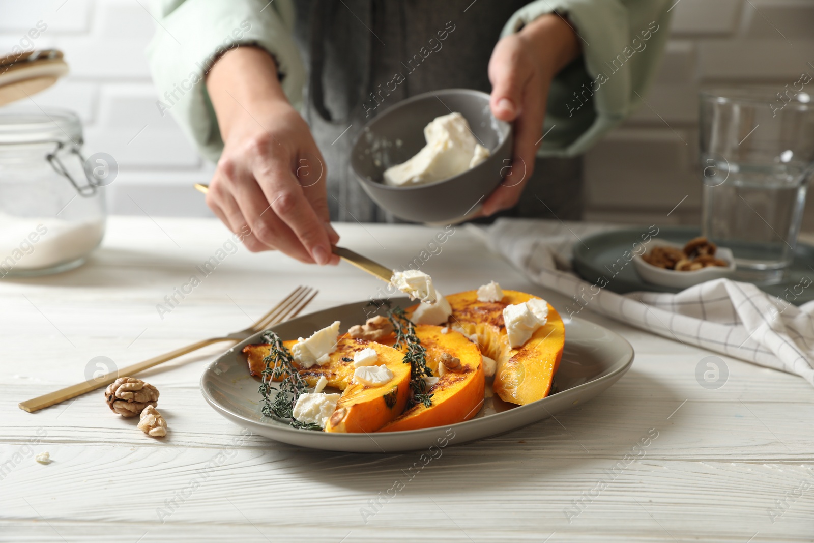 Photo of Woman putting cheese on baked pumpkin slices at table, closeup