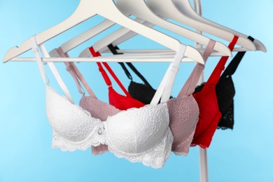 Hangers with beautiful lace bras on rack against blue background. Stylish underwear