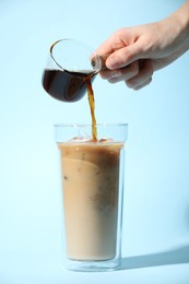 Photo of Woman making iced coffee on light blue background, closeup