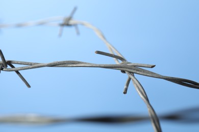 Photo of Metal barbed wire on light blue background, closeup