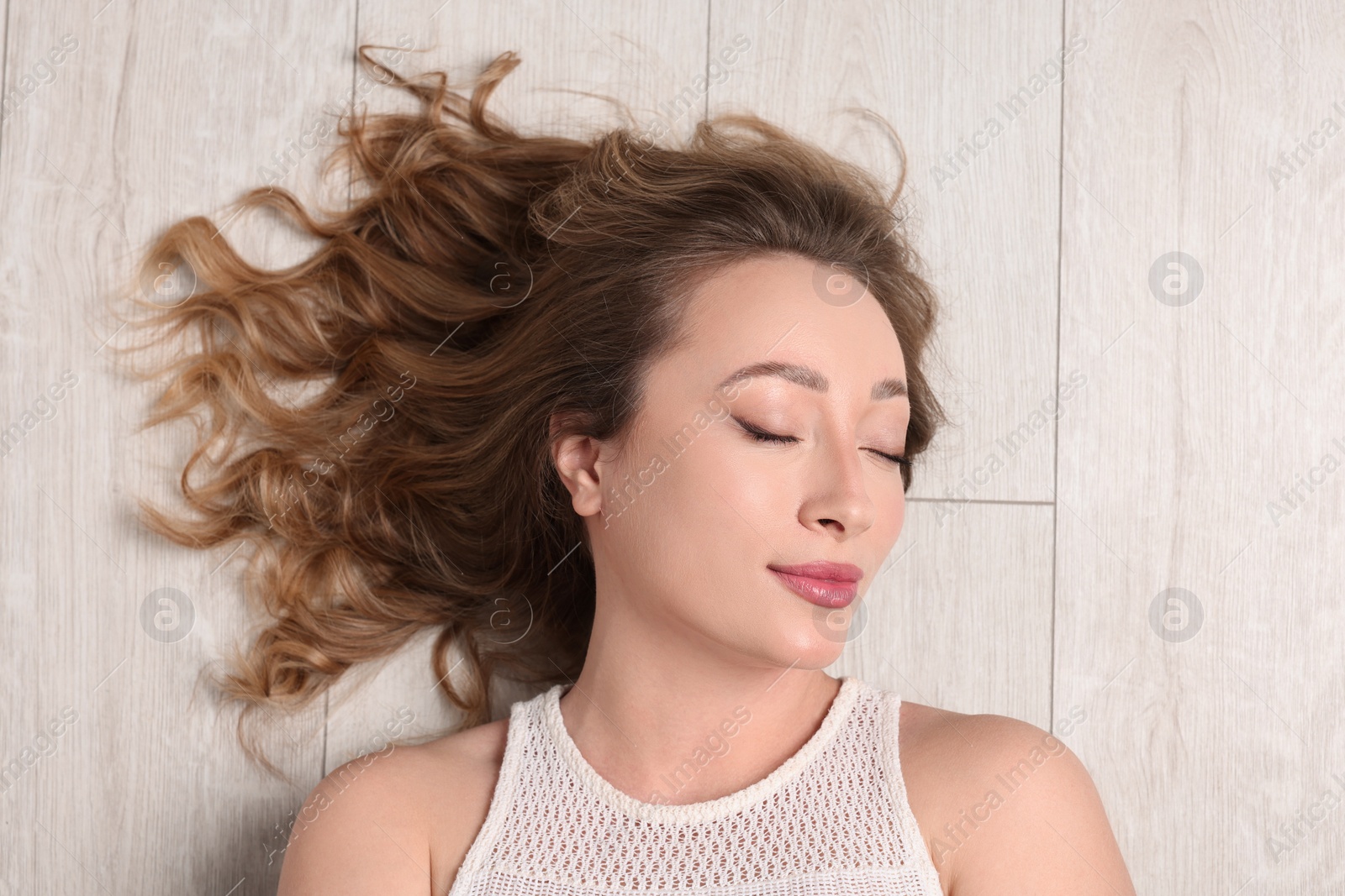 Photo of Portrait of beautiful woman with closed eyes on wooden floor, top view