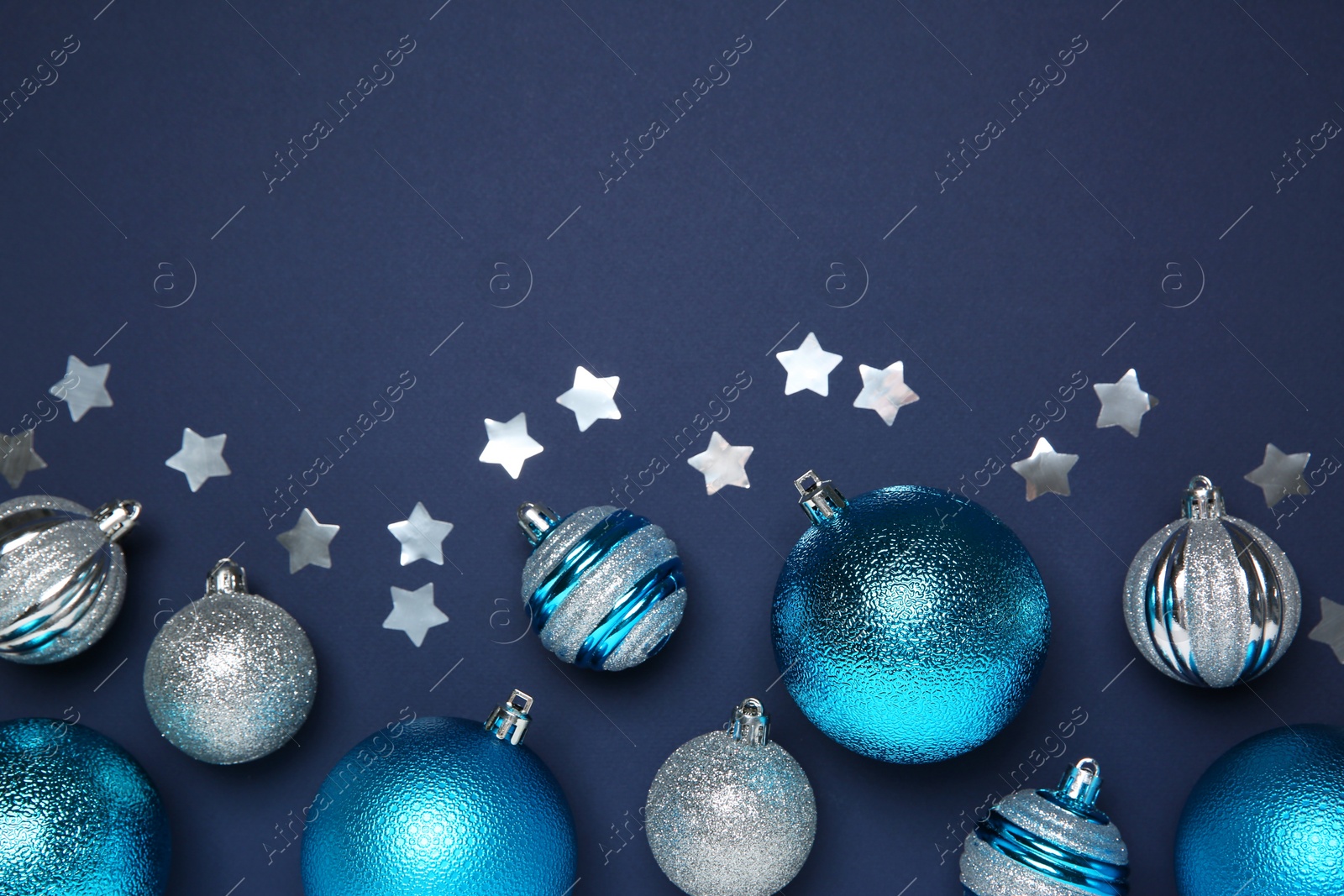 Photo of Christmas balls and confetti on dark blue background, flat lay. Space for text